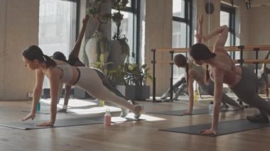 Aktif giyimli bir grup genç kadın parlak ferah fitness stüdyosunda paspaslar üzerinde pilates yapıyor.