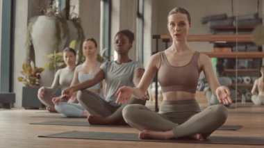 Aktif kıyafetli, yoga minderlerinde poz veren ve meditasyon yapan bir grup genç kadın.