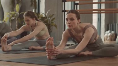 Fitness stüdyosunda paspaslar üzerinde esneme egzersizleri yapan genç ve formda kadınların yavaşlaması.