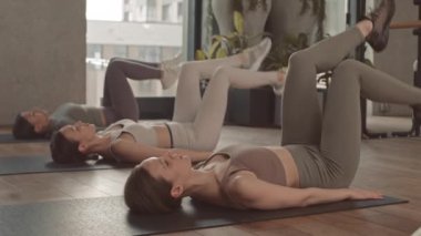 Parlak fitness stüdyosunda yoga minderleri üzerinde uzanırken karın kası egzersizi yapan genç kadınların yavaşlaması.