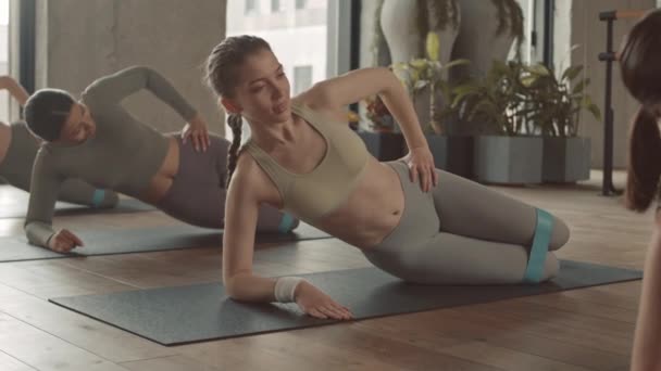 现代健身演播室中穿着运动服 头戴电阻带躺在垫子上的年轻女运动员的运动速度 — 图库视频影像