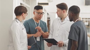 İki doktor ve iki erkek hemşirenin hastane koridorunda tartıştıkları ve panodaki hastanın sağlık kartına baktıkları orta derece ağır tıbbi ekip.