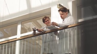 Laboratuvar önlüklü birkaç doktor modern klinikteki tırabzanlara dayanan tıbbi belgelere bakıyor.