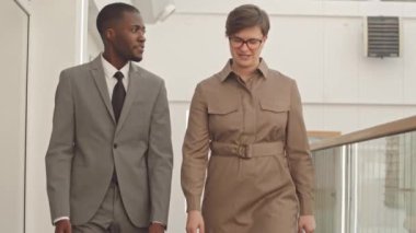 Çağdaş ofis koridorunda yürüyen başarılı çok ırklı iş çifti yavaş yavaş sohbet ediyor.