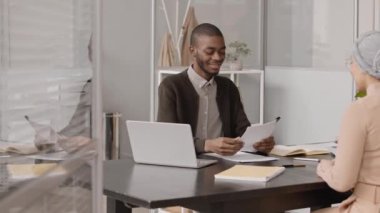 Genç Müslüman kadının, özgeçmişini ya da gizli mektubunu genç Afrikalı Amerikalı HR yöneticisine verip, elini sıkarak ve ofisten ayrılırken orta derecede yavaşlaması.