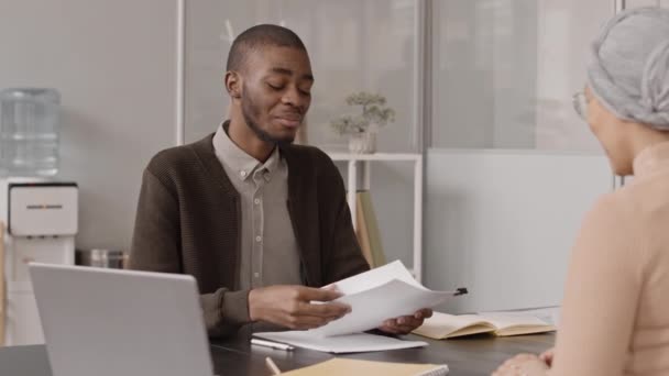 フレンドリーなアフリカ系アメリカ人採用マネージャーの中低速面接候補者と彼女の履歴書を読んで オフィスでお互いの前に座って — ストック動画