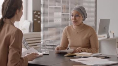 Başörtüsü takmış, başvuru yapanla görüşen, ofis masasında yan yana oturan Müslüman bir kadının orta derecede yavaşlaması.