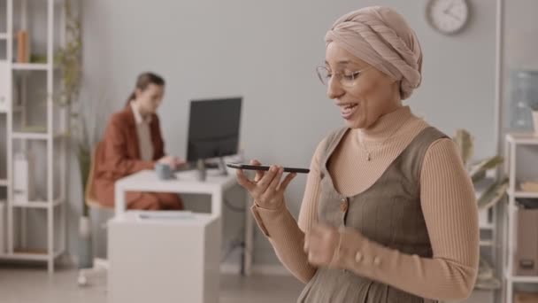 사무실에 스마트폰으로 메시지를 녹화하는 열정적 이슬람 여성의 사무실에 그녀의 컴퓨터에서 — 비디오