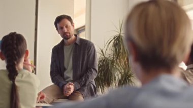 Modern sınıfta masa başında otururken orta yaşlı bir erkek öğretmenin bir grup ortaokul öğrencisine konuşması.