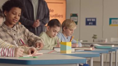 Ders sırasında öğretmenleri dinlerken kitaplara not alan çoklu etnik kökenli öğrencilerin yavaşlığını bastır.