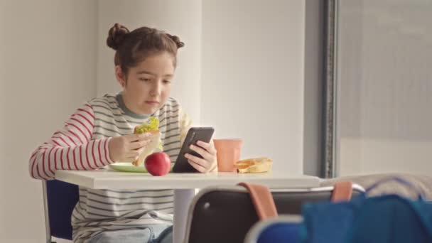 11岁女学生在学校食堂吃午饭时用智能手机打滚的慢动作 — 图库视频影像