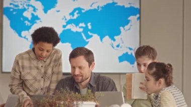 Çok ırklı okul öğrencileri ve erkek öğretmenleri bilgisayar ekranına bakıp coğrafya dersinde tartışıyor.