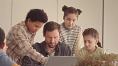 Orta yaşlı erkek öğretmen ve çok ırklı ortaokul öğrencilerinin yavaş yavaş dizüstü bilgisayara bakmaları ve ders sırasında tartışmaları.