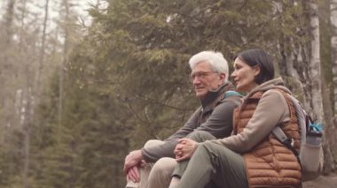 Olgun beyaz bir çiftin, bahar ormanında suyun kenarında kameraya gülümseyen yavaş portresi.