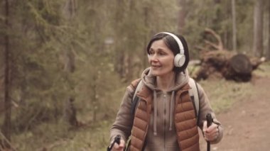 Kuzeyli güzel bahar ormanlarında tek başına yürürken enerjik, olgun kulaklıklı bir kadının yüksek sesle şarkı söylemesi.