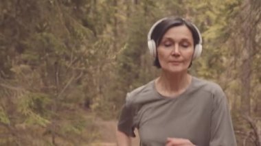 Kulaklıklı, aktif ve olgun bir kadının sabahın köründe ormanda tek başına koşması.