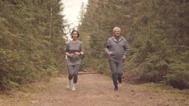 Aktif giyimli, olgun, beyaz bir çiftin ormanda birlikte koşu yaptığını görüyorum.