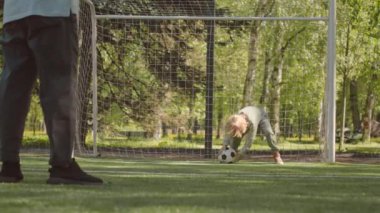 7 yaşında tatlı bir çocuk ve babası yazın futbol sahasında futbol oynuyorlar. Ağ başında durup futbol oynayan çocuk.