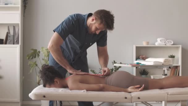 Langzame Mannelijke Fysiotherapeut Doet Tape Applicatie Rug Van Jonge Vrouw — Stockvideo
