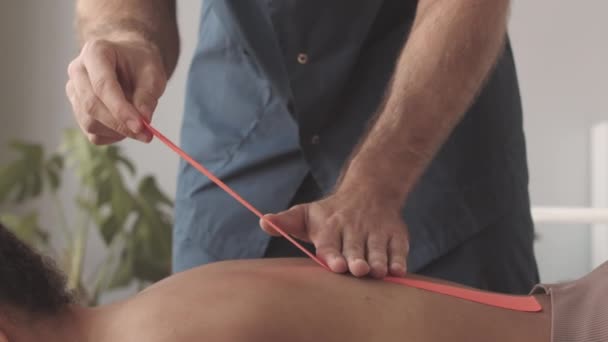 Långsam Oigenkännlig Manlig Kinesiolog Tillämpa Röda Band Baksidan Kvinnlig Patient — Stockvideo