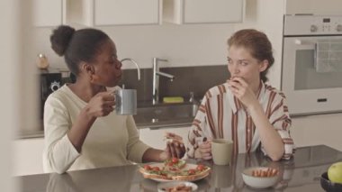 Modern minimalist stil mutfaktaki masada ev yapımı sandviçleri yerken sohbet eden keyifli, genç lezbiyen çiftin orta yavaşlığı.