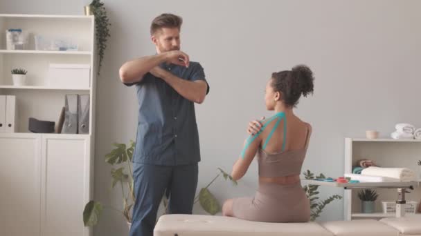 Медленно Мужчина Физиотерапевт Показывая Упражнения Молодой Женщины Biracial После Прикрепления — стоковое видео