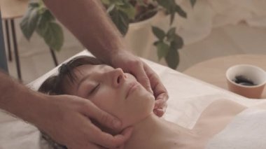 Lüks kaplıcalarda profesyonel masör tarafından yapılan yüz masajı sırasında gözleri kapalı uzanan güzel bir kadının yavaşlığı.