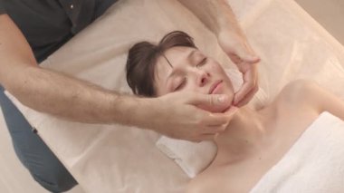 Lüks kaplıcalarda yüz masajı yaptıran genç, beyaz bir kadının yavaş görüntüsü.