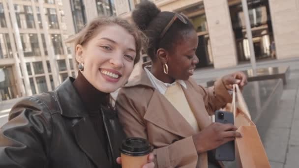 二人の若い美しい多民族の女性のPovハンドヘルドSlowmo彼ら自身の笑顔とカメラで話してのビデオを記録 一緒に買い物をした後 屋外のベンチに座って — ストック動画