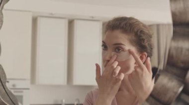 Göz bantları altında aynaya bakıp gülümseyen heyecanlı, etnik çeşitliliğe sahip iki genç kadının belini yavaşça bük.