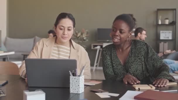 坐在写字台上讨论设计项目构想的两位年轻 多样化的女同事的速度中等 — 图库视频影像