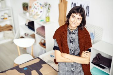 Gülümseyen yaratıcı genç moda tasarımcısının portresi stüdyosunda duruyor ve kameraya bakıyor.