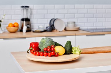 Modern mutfaktaki ahşap masada taze sebzeler salata için hazırlanıyor.