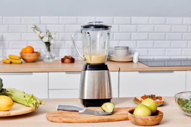 İçinde taze kokteyl bulunan modern elektrikli blender meyve ve sebzelerin arasında masada duruyor.