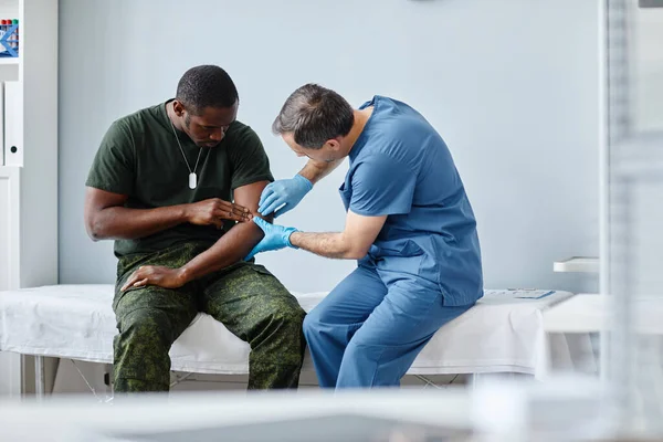 戴防护手套的专业创伤专家触诊年轻非裔美国士兵受伤的胳膊 — 图库照片