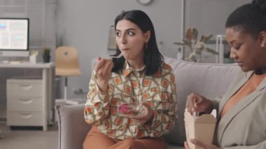 Çağdaş ofisteki kanepede birlikte yemek yerken konuşan iki farklı kadın iş arkadaşının belini yavaşça yukarı kaldır.