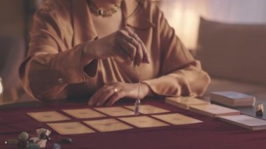 Tarot kartlarının üzerinde sarkacı tutan tanınmayan bir falcı yavaşladı.