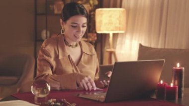 Dizüstü bilgisayardaki video seansı sırasında müşterilerine tarot kartları dağıtan Orta Doğulu genç falcı belini kaldır.