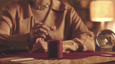 Tanımlanamayan bir falcı, kırmızı kadife kumaşın üzerine tarot serpiştirilmiş parmaklarıyla mum söndürüyor.