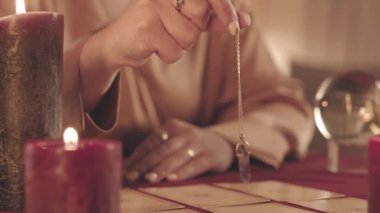 Tarot kartlarının üzerinde sarkacı tutan tanınmayan bir falcının yavaş çekimleri masaya yayıldı.