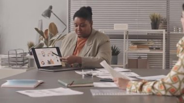 Orta Doğulu kadın işverenlere pazarlama istatistikleri hakkında konuşurken dizüstü bilgisayarda slayt sunumu yapan Afrikalı Amerikalı kadının belini yavaş yavaş kaldırın.