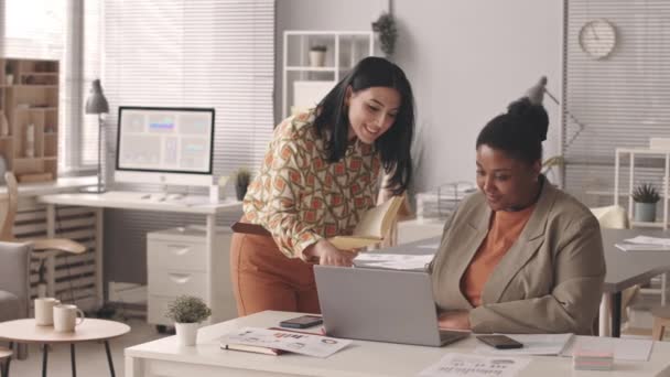 两位年轻的多族裔女同事在现代办公室里一起工作 看着手提电脑屏幕 聊着话 动作有点慢 — 图库视频影像