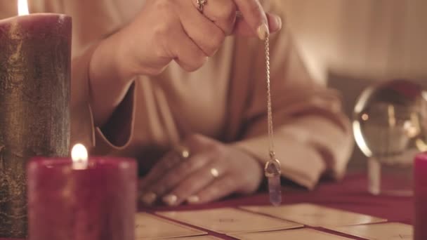 テーブルの上に広がるターロットカードの上に振り子を保持している認識できない宝石占い師の作物の遅い閉鎖 — ストック動画
