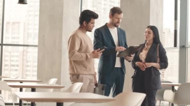 Akıllı, çok ırklı üç iş arkadaşından oluşan orta boy bir yavaşlama. Panoramik pencereli kafede dururken iş belgelerini tartışıyorlar.