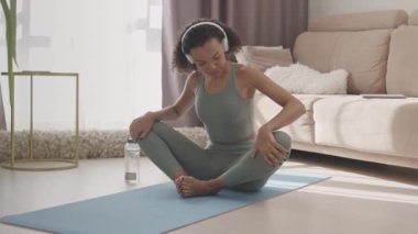 Aktif giyinen ve kulaklık takan, evde kelebek esneten yavaş, çift ırklı bir kız.