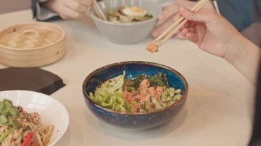 Kafede Asya yemeği yerken, arkadaşlarıyla ya da iş arkadaşlarıyla yemek yerken, yemek çubuğu kullanan, tanınmayan esmer kadının yavaş çekimleri.