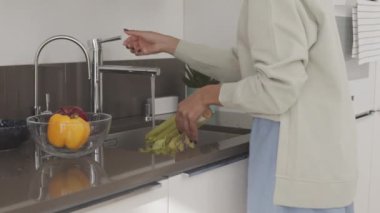 Evde yemek pişirirken kereviz ve diğer taze meyve ve sebzeleri yıkayan çekici genç kadının orta yavaş izini sürüyorum.