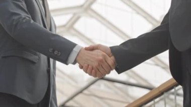 İki tanınmayan girişimcinin düşük açılı orta bölüm yavaşlaması. Takım elbiseli iki girişimci el sıkışarak ve sohbete başlayarak modern iş merkezinde buluşuyorlar.