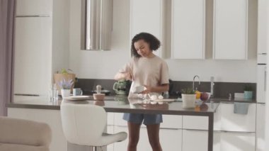 Sabah kahvaltısı için çırpılmış yumurta pişiren gülümseyen melez genç bir kız.