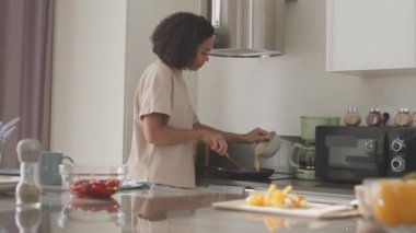 Evde kahvaltıda çırpılmış yumurta pişirirken karışık yumurta ve sütü klozetten kızartma tavasına döken melez genç bir kadın.